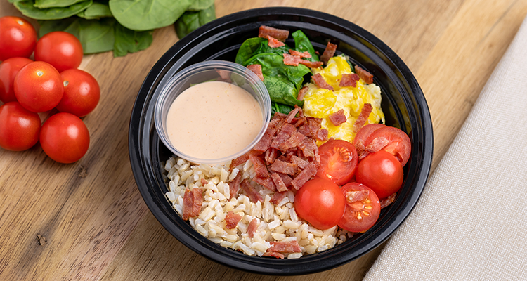 Overhead view of a bowl containing rice, tomatoes, eggs, spinach, and bacon