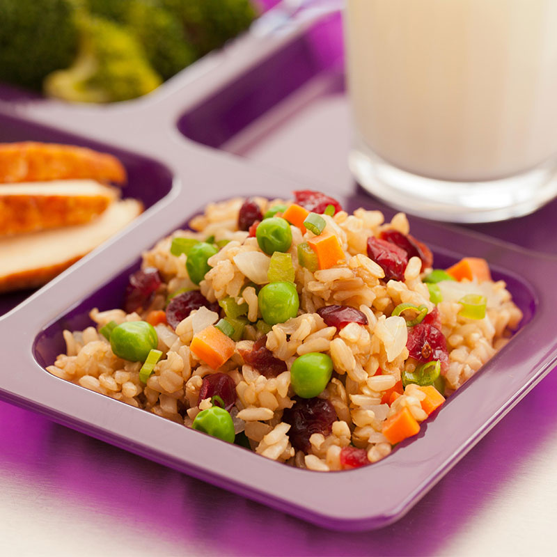Close up view of cranberry brown rice with veggies on a purple school lunch tray.