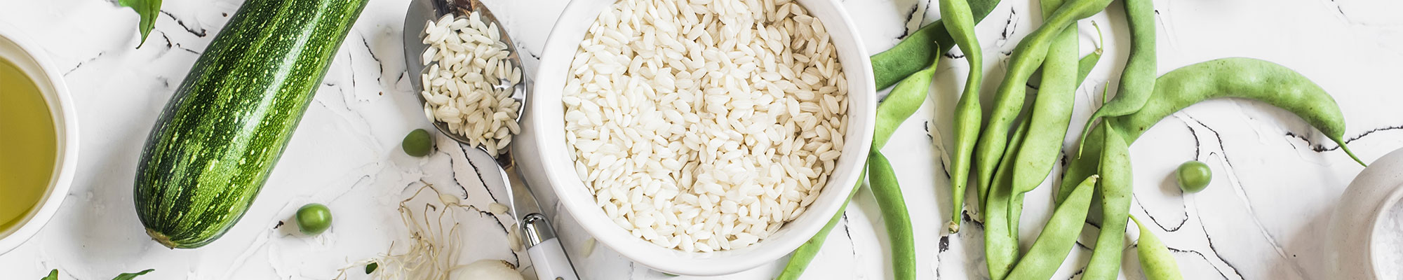 Overhead view of raw rice grains in a bowl surrounded by vegetables.