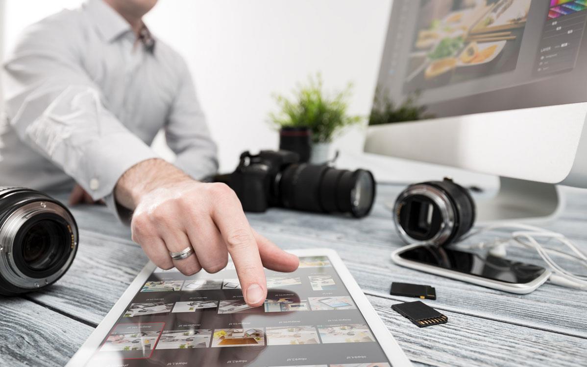 Man chooses-photo-from-contact-sheet, camera lenses, phone, and computer monitor on desk