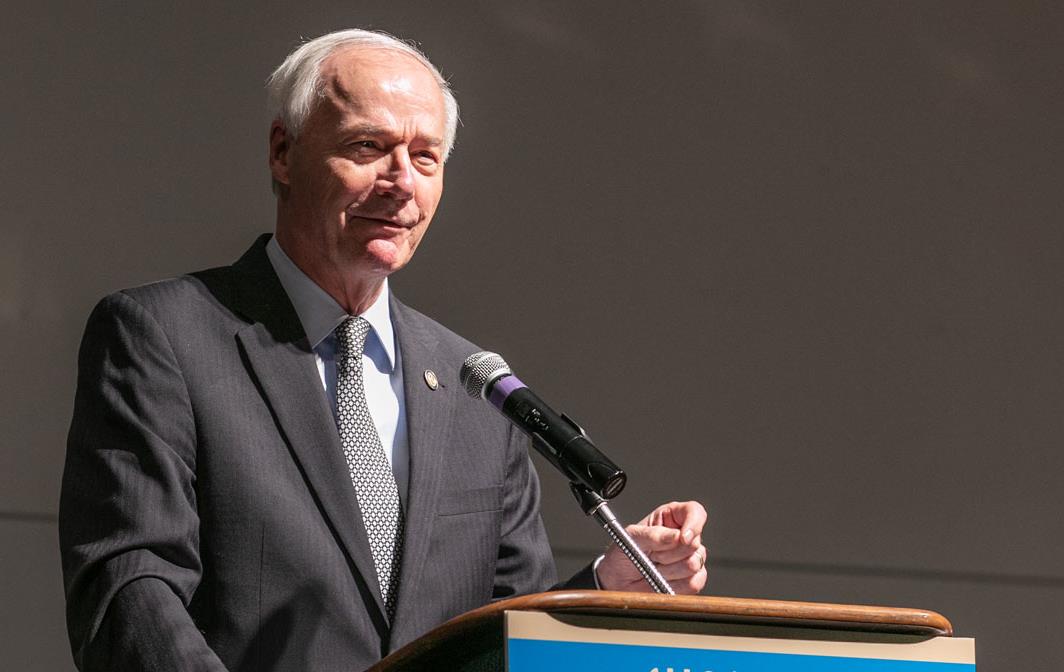 Older white man wearing business suit stands in front of podium with USA Rice Outlook Conference Little Rock AR sign