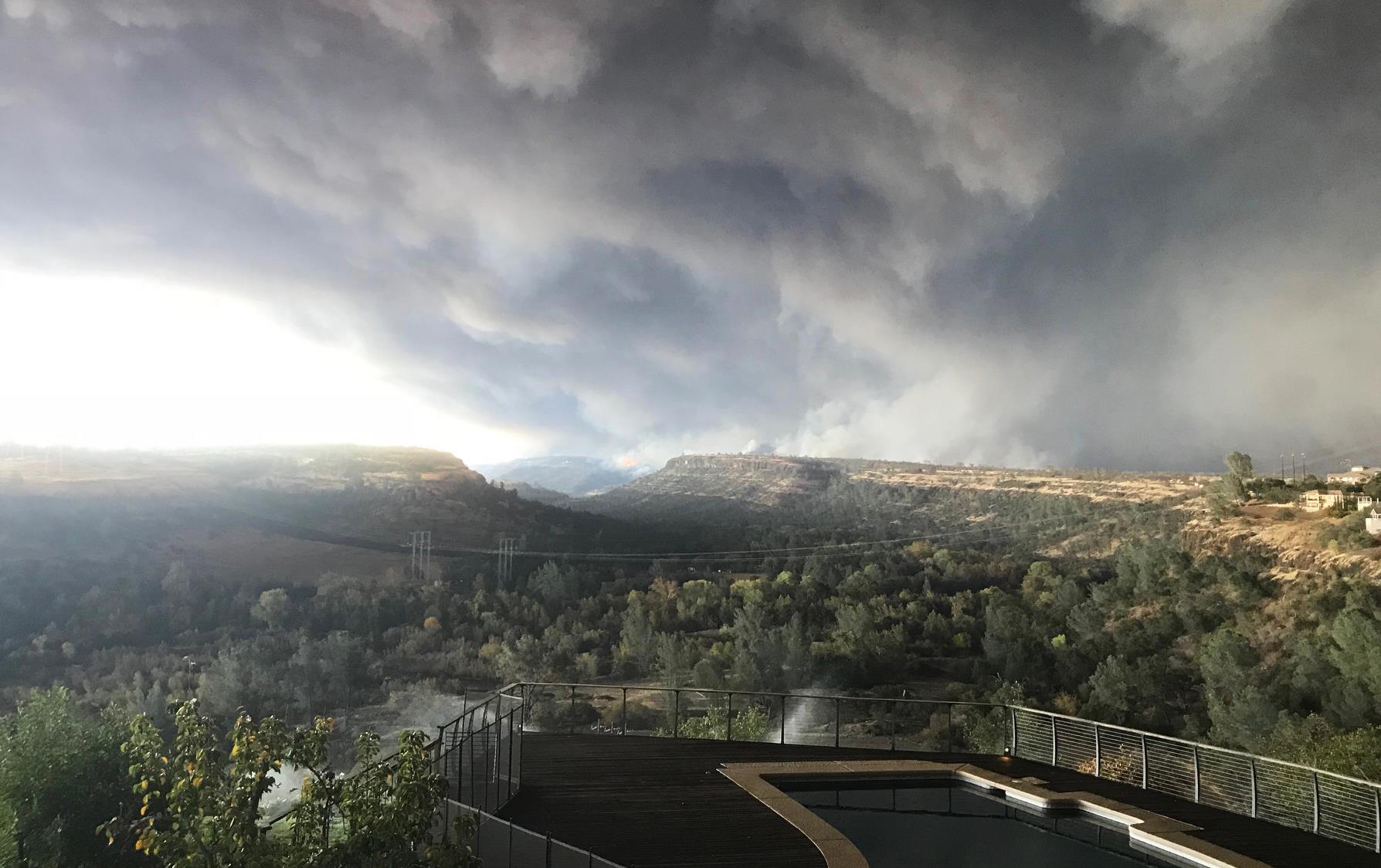 CA Camp Fire, Logan Wilson photo, mass of smoke covers the whole sky above mountains (background) and tree-filled valley (foreground)