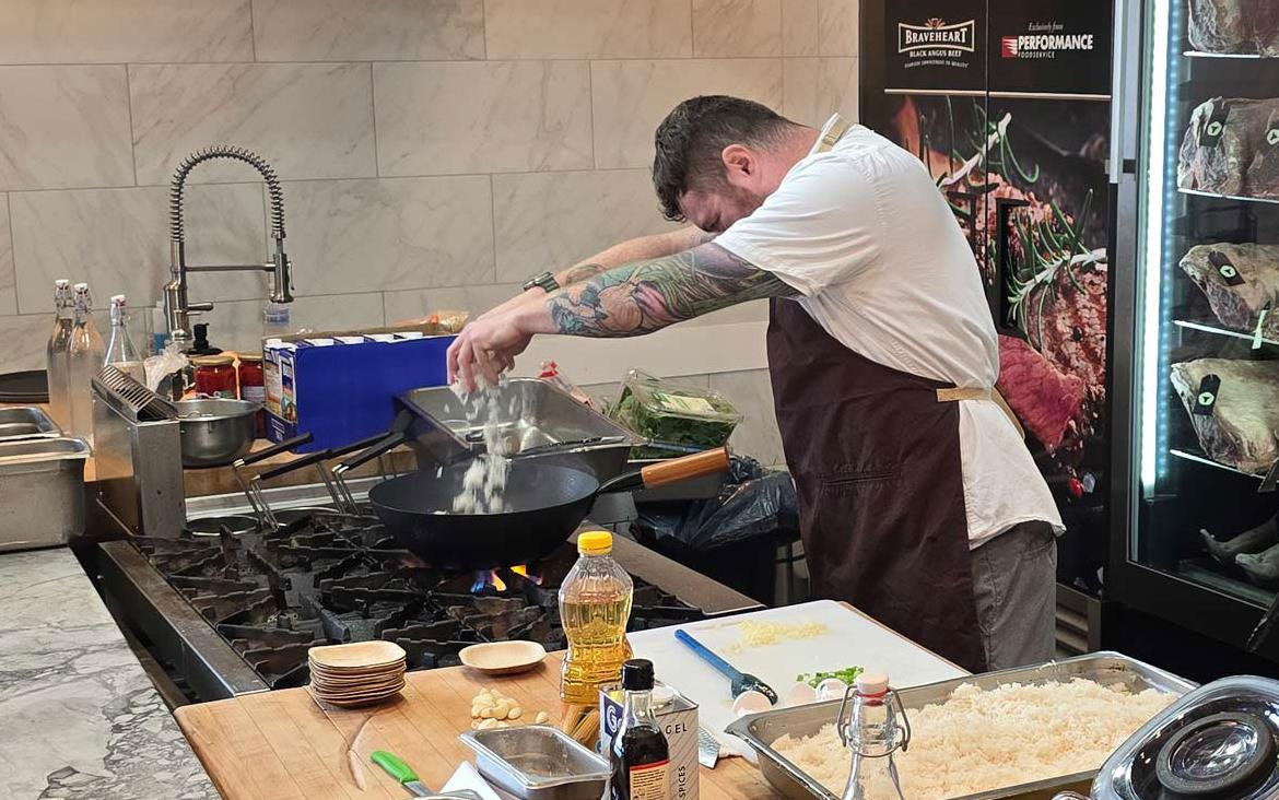 Chef-Hari-Cameron-adding-rice-to-wok on stove over open flame