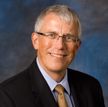 White man with gray hair wearing glasses and a dark business suit and brown tie