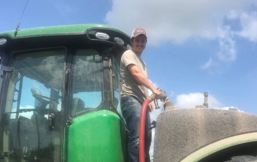 Young man wearing ballcap fueling up combine