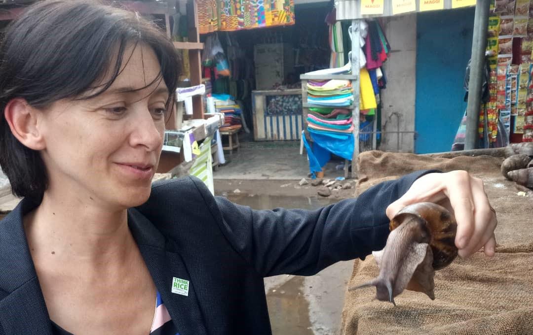 Woman wearing black blazer with Think Rice lapel pin visits an outdoor food market and holds gigantic snail