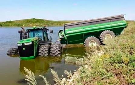 Green tractor and cart stuck in in flooded ditch