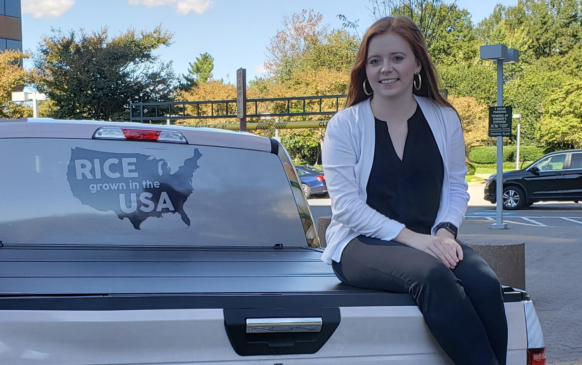 Red-haired woman sits on back of Think Rice pickup truck