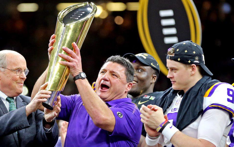 LSU Coach Joe Orgeron holds gold championship trophy while team members look on