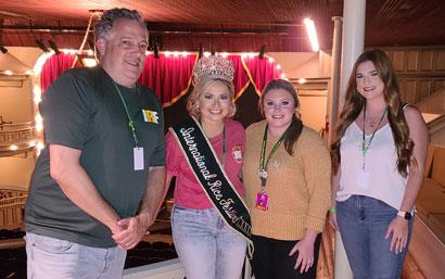 One man stands next to three women, one wearing a crown