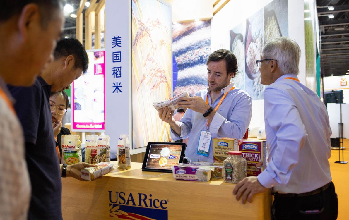 Trade-show-booth, group of men examine rice products displayed on table