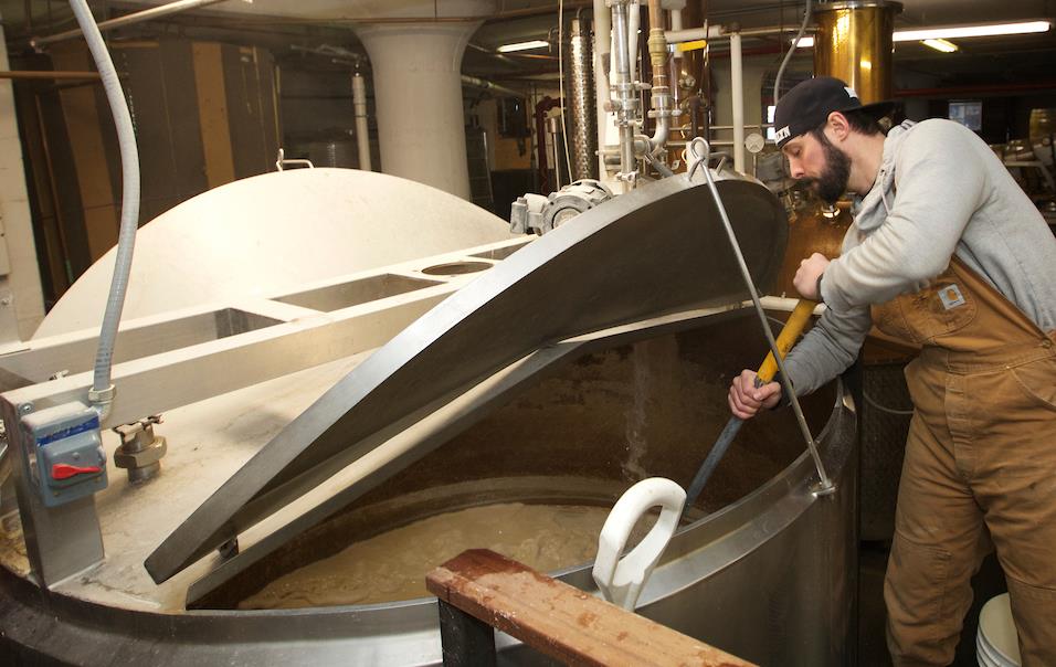 Soju brewer Brandon Hill wearing brown overalls stirs mash in large metal vat, Clay Williams photo-190124