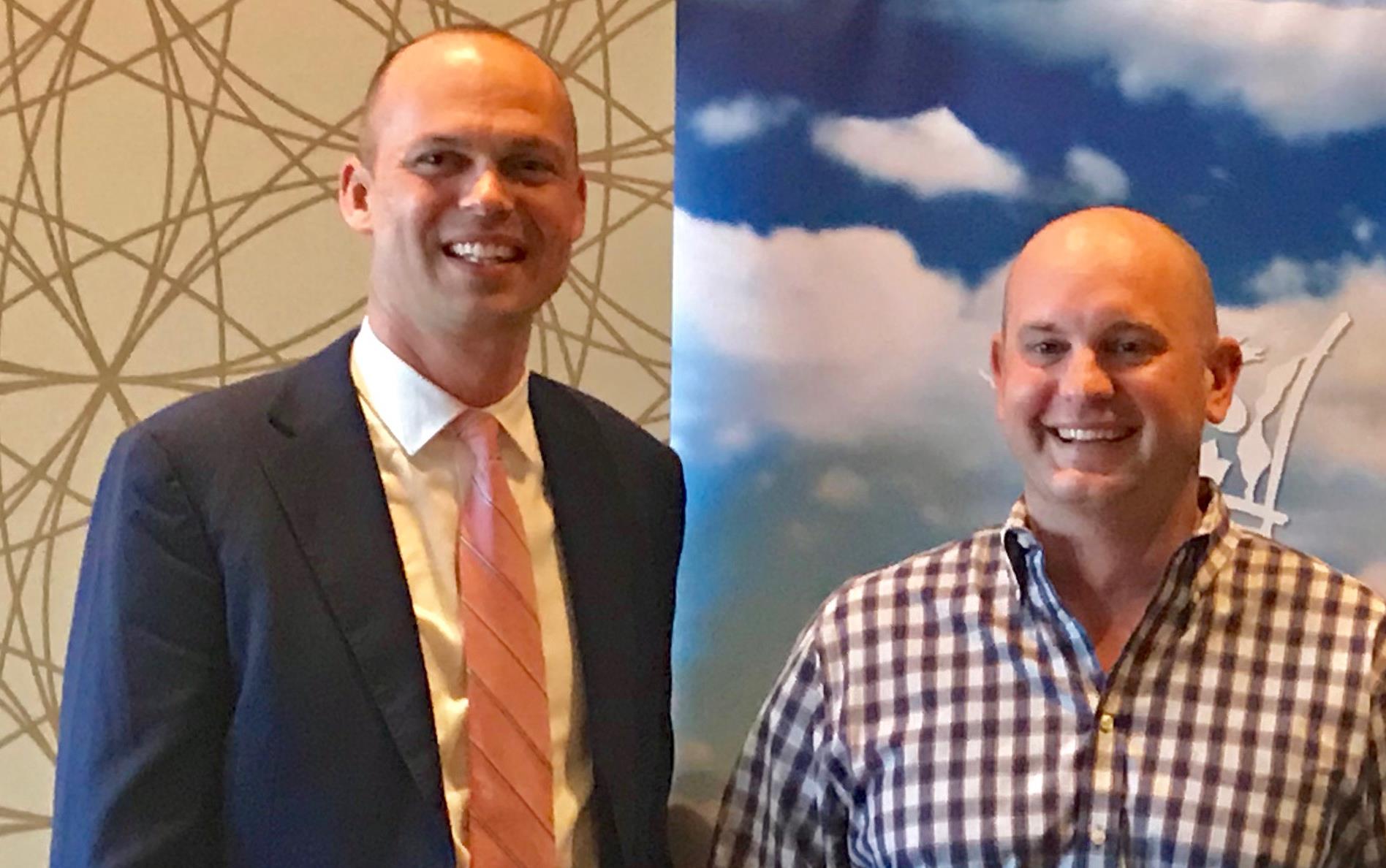 Two men stand in front of poster of blue sky with puffy white clouds