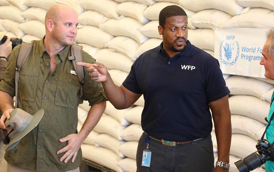 Men stand in front of pallets of bags of rice