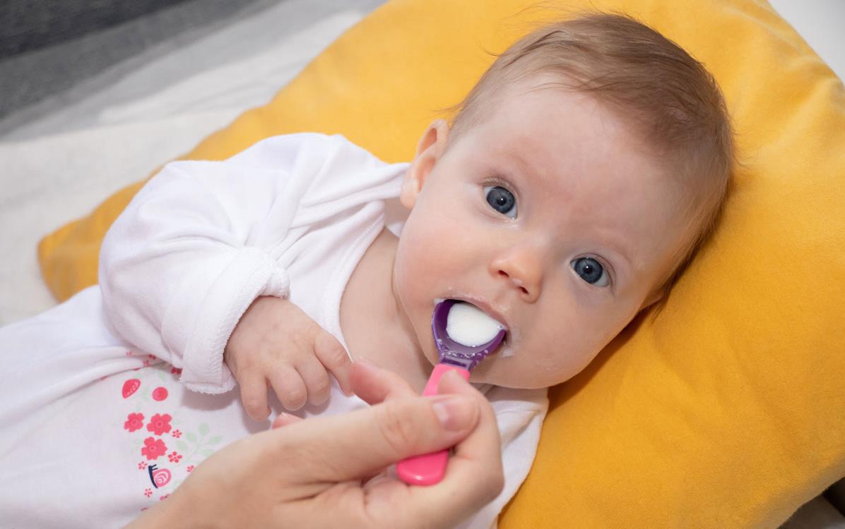 Baby lying on gold pillow-being-fed-rice-cereal on a pink spoon