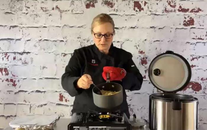 Female chef holds pot filled with rice, rice cooker beside the stovetop