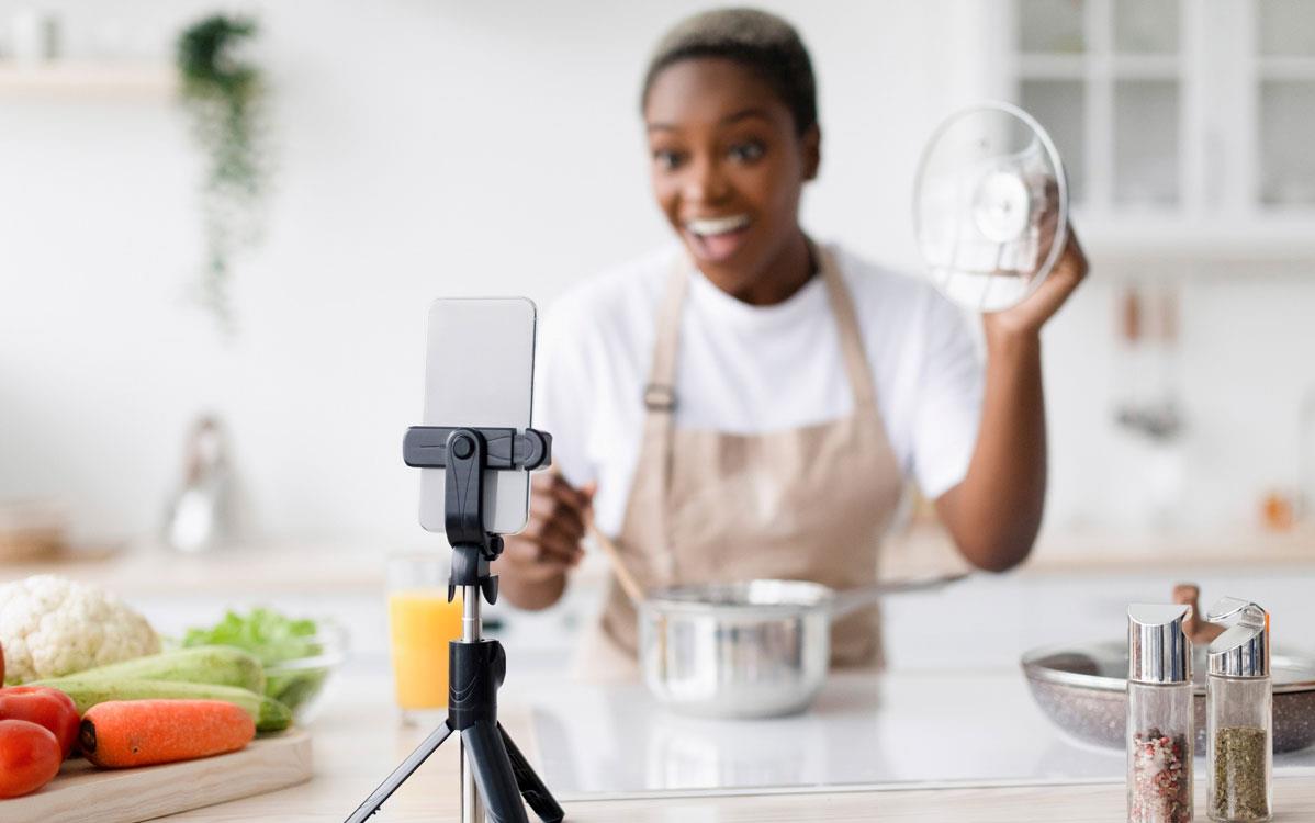 Food-blogger-filming cooking video in her kitchen on a cell phone mounted on a tripod