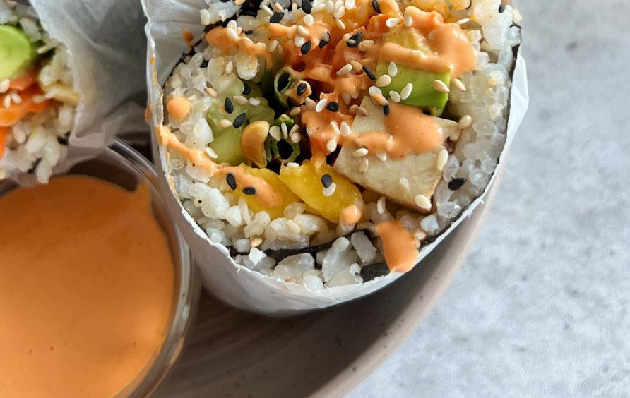 Colorful veggie sushi burrito on a plate with orange dipping sauce