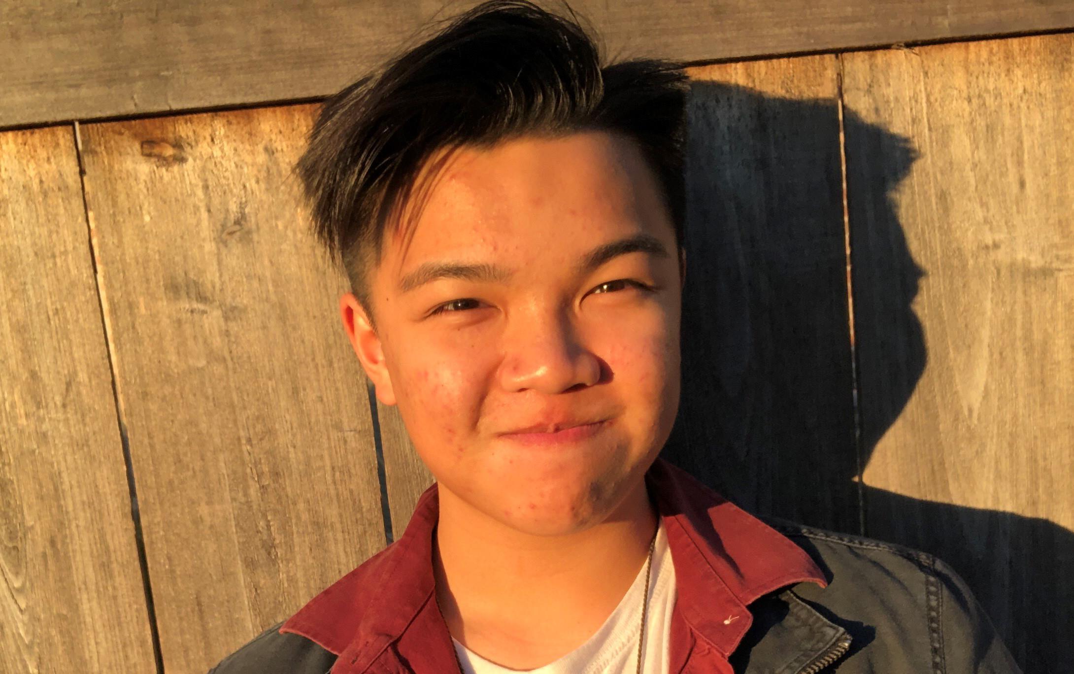 Young, casually dressed Asian man stands in front of wood fence