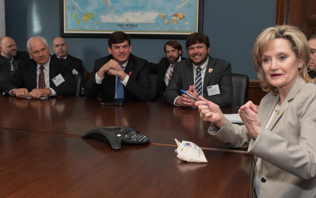 White woman holding pen and gesturing with hands holds court at table of white men wearing suits