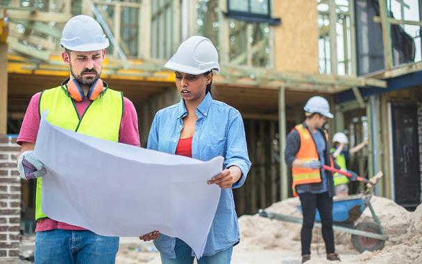 Construction-Workers wearing hard hats look at plans