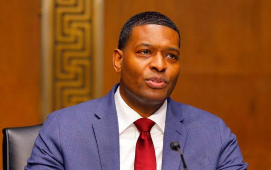 Black man wearing business suit sits at table, speaking into microphone, AgriPulse-photo