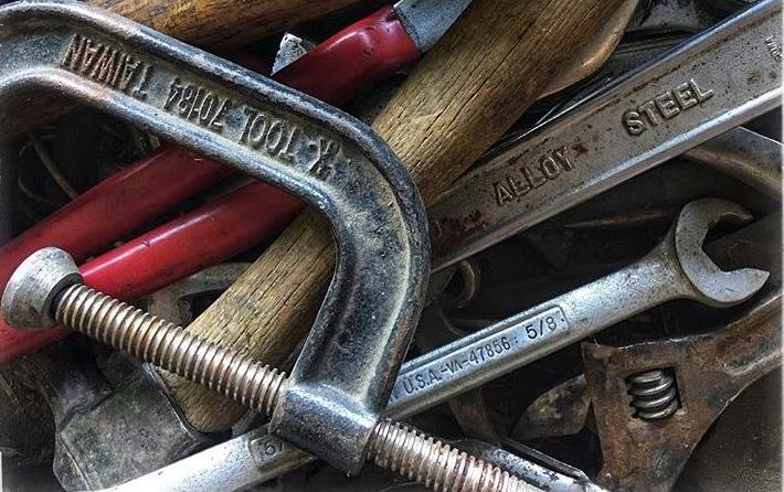 Farm tools in a toolbox including a vise, wrenches, and wooden handled implements, photo by M. Sligar