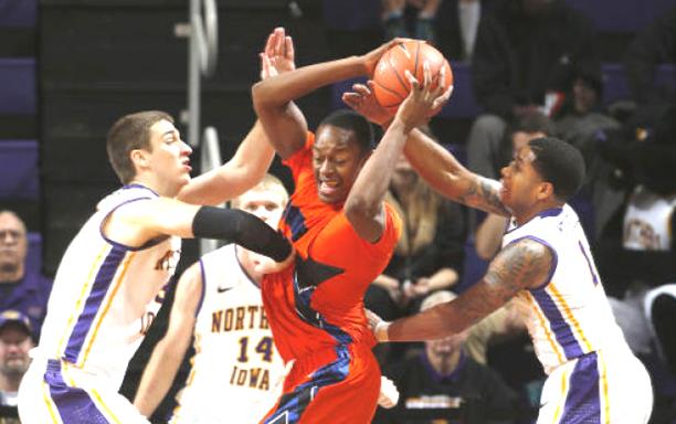 Three basketball players in white/purple uniforms pressure single player in orange with the ball