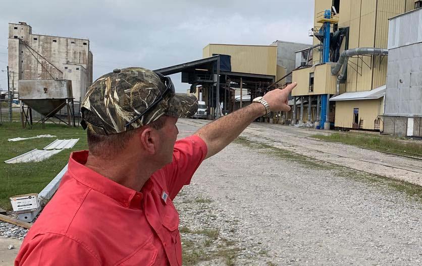 Man wearing camo ballcap points to rice milling facility