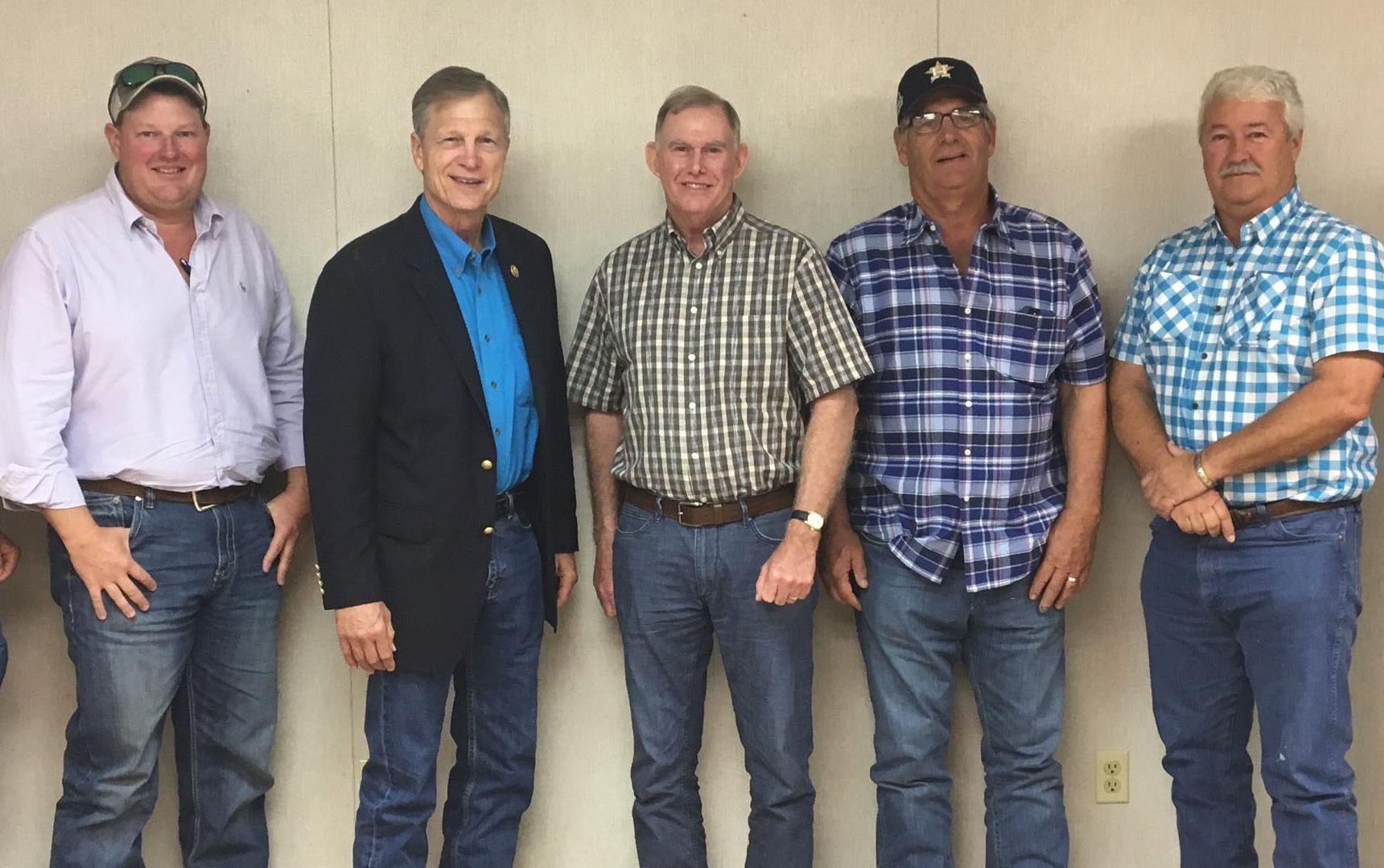 Line up of white men in button-down shirts and jeans, standing against beige wall