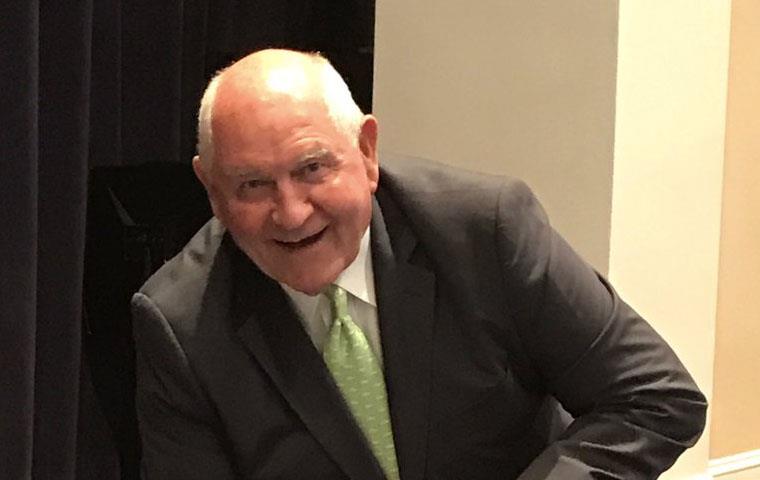 Secretary Perdue & UGA bulldog, man wearing suit kneels down next to white bulldog