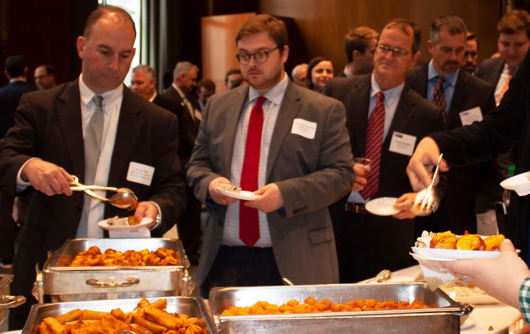 Buffet-line, chafing dishes filled with food, long lines of people on either side of table serving themselves