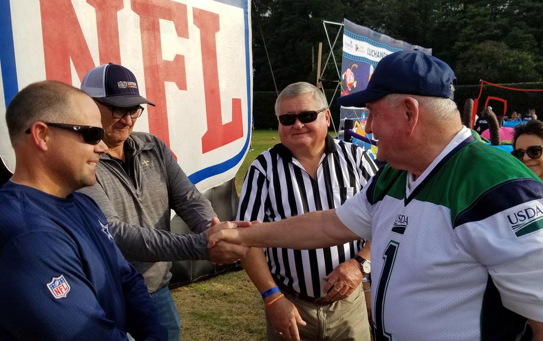 Men dressed in football jerseys shake hands in front of large NFL sign