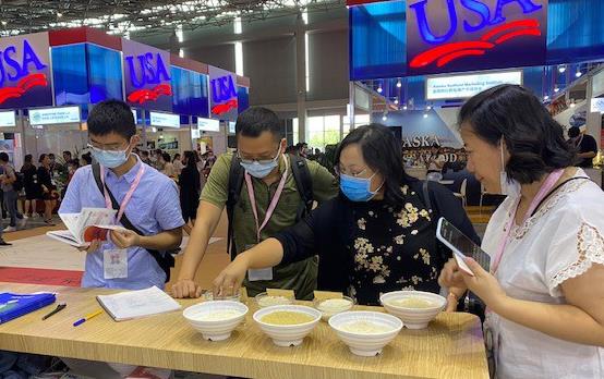 People wearing face masks stand around table filled with rice samples in white bowls