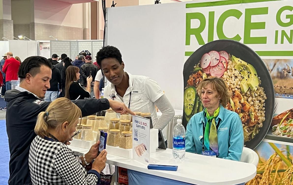 2023-SIAL-Las-Vegas,-A.-Grigsby-&-J.-Bryant-at-the-booth, talking with visitors who are taking cellphone photos of rice