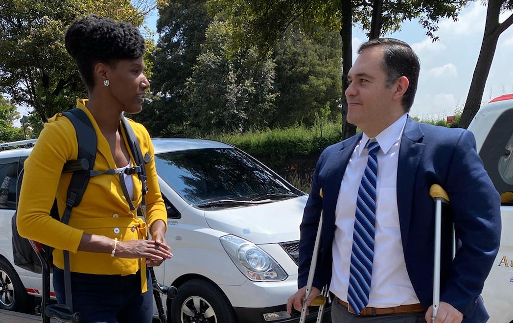 A woman and man, both on crutches, stand on sidewalk talking