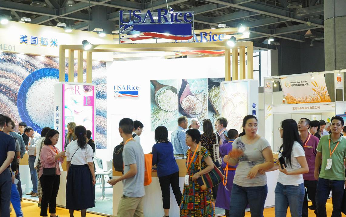 Many people walk around USA Rice trade show booth with signage and lots of rice photos