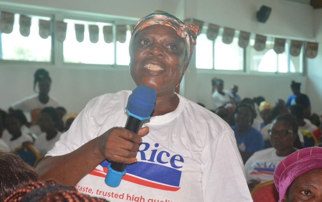 African woman, wearing white t-shirt with USA Rice logo, speaks into blue microphone