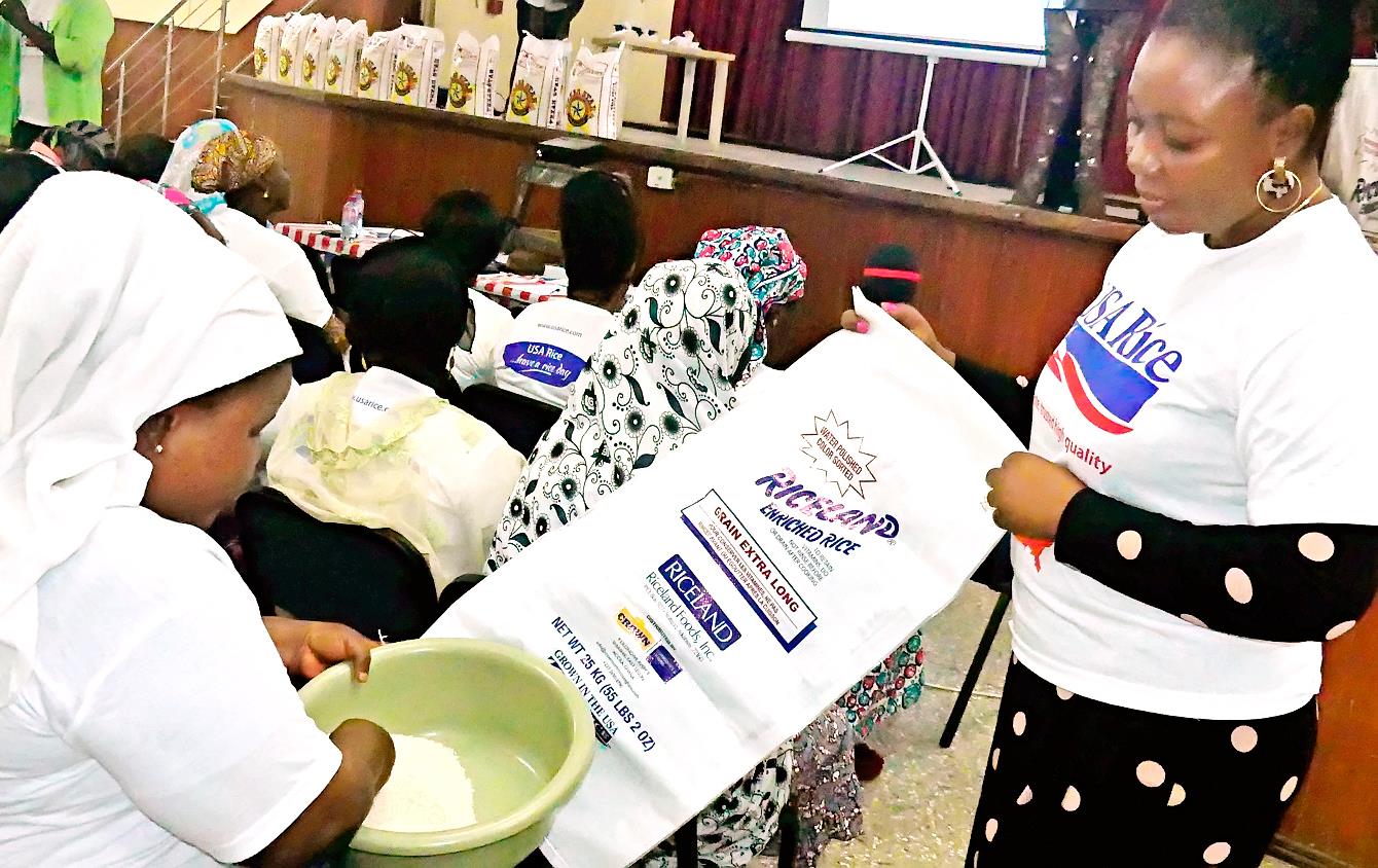 One woman stands, holding large empty rice bag while another woman who