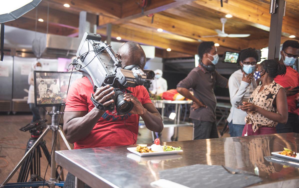 Man filming close-up of rice dish on stainless steel table, people wearing face masks in background