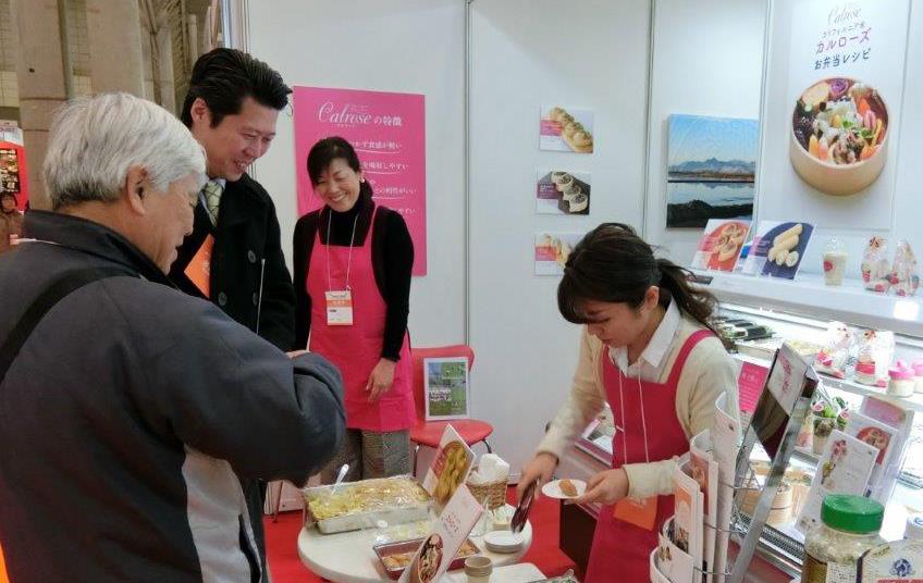 Japanese Supermarket Trade Show, women wearing pink aprons serve rice samples to two men standing in front of display case