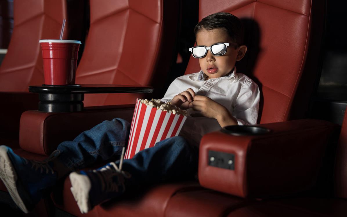 Young boy wearing glasses, eating-popcorn-in-movie-theater