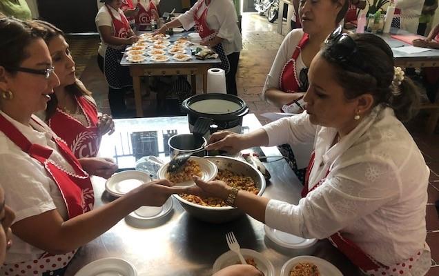 Women wearing red aprons with text "Club Arroz" dish out rice samples for taste testing