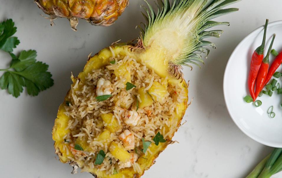 Pineapple-Shrimp-Fried-Rice, along with whole pineapple, plates of limes, lemons, red peppers, and green onions