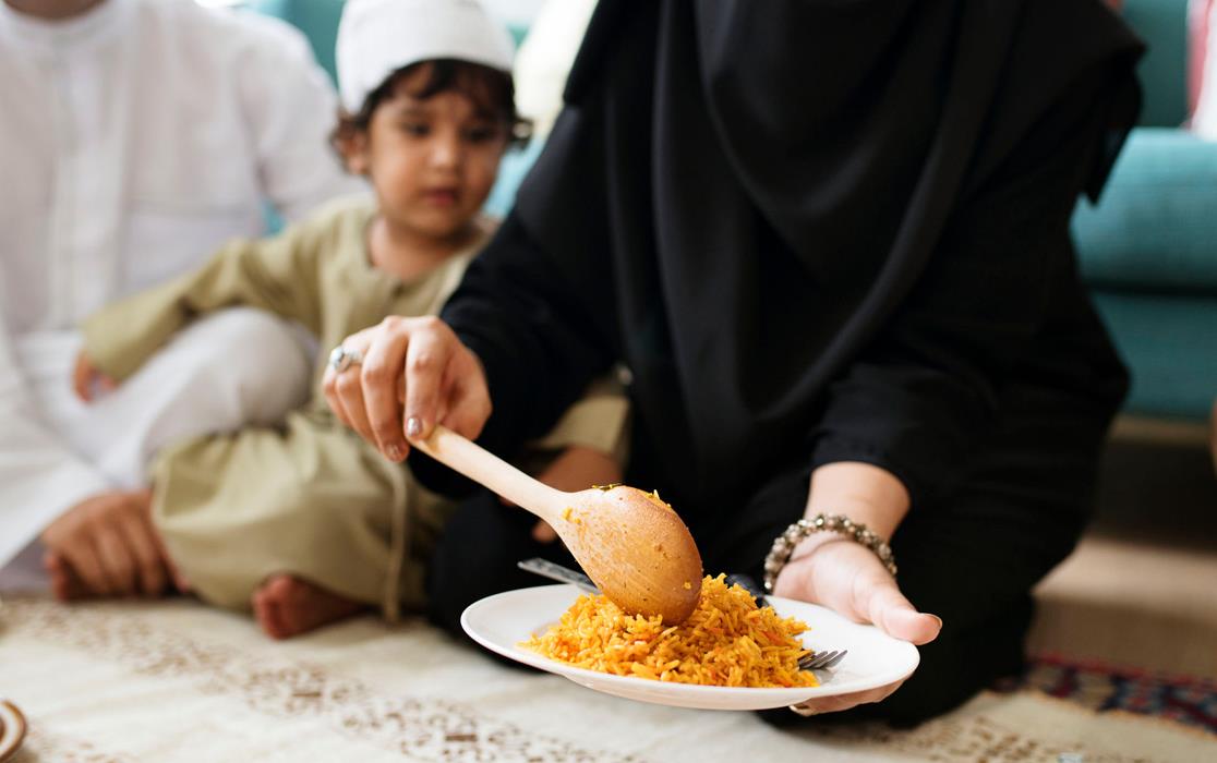 Woman serves Ramadan rice meal, child and man in background