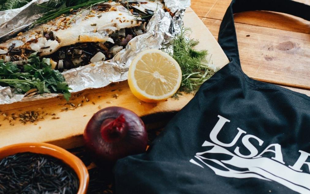 Sea-Bass stuffed with wild rice, wrapped in foil, on cutting board, next to USA-Rice-Apron