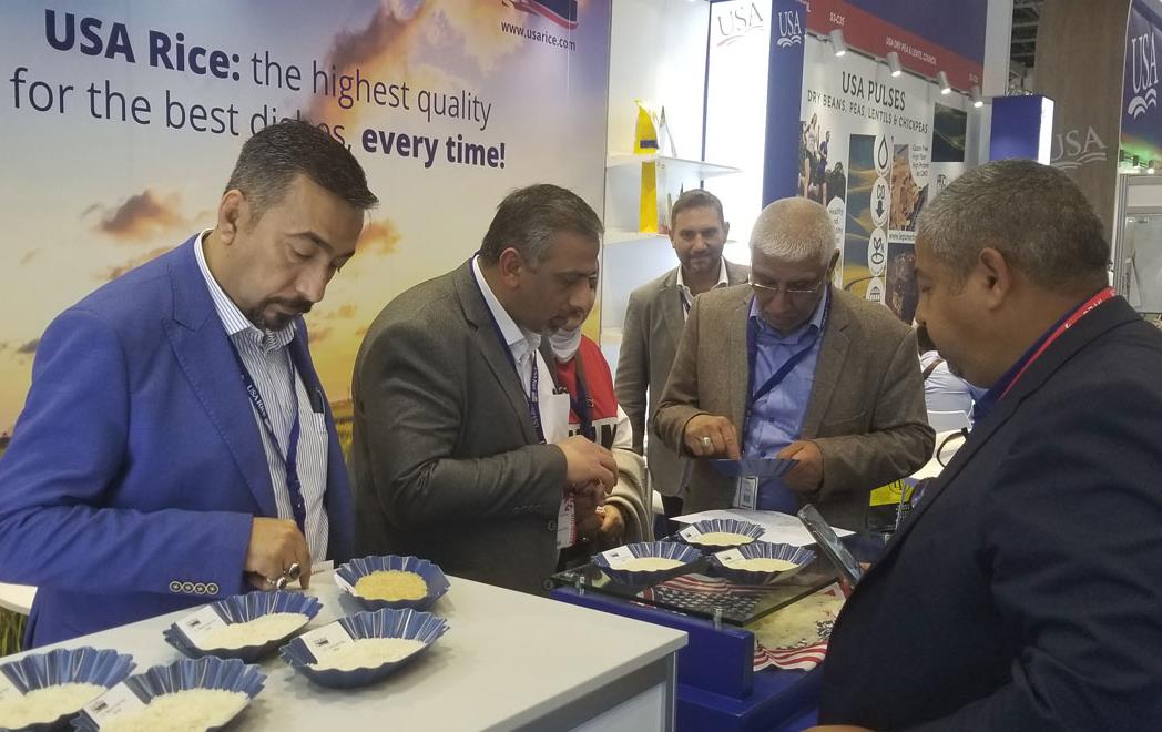 USA-Rice-Booth-at-Gulfood-Show, group of men stand at table examining rice samples in small blue bowls