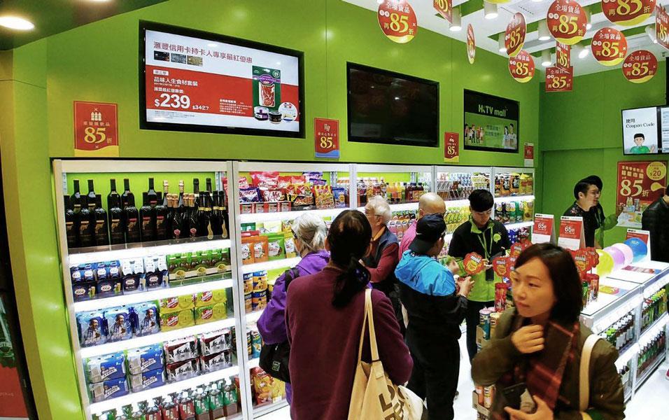 People stand in line at a small package store, lime green walls with circular banners hanging from the ceiling