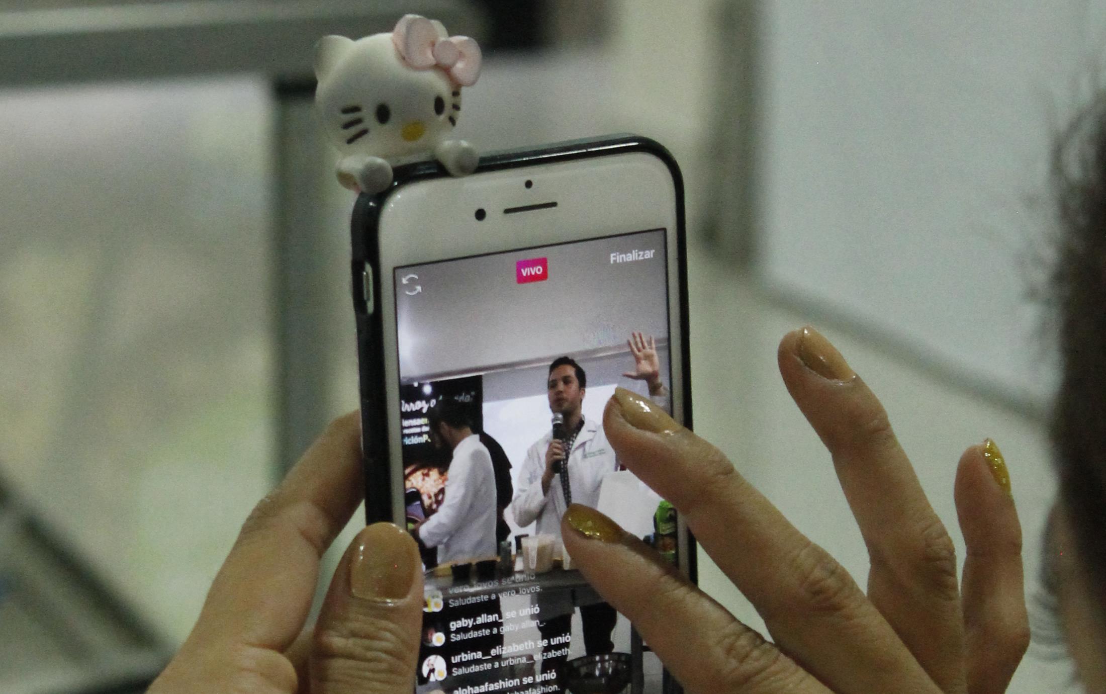 Hands holding cellphone adorned with Hello Kitty figurine