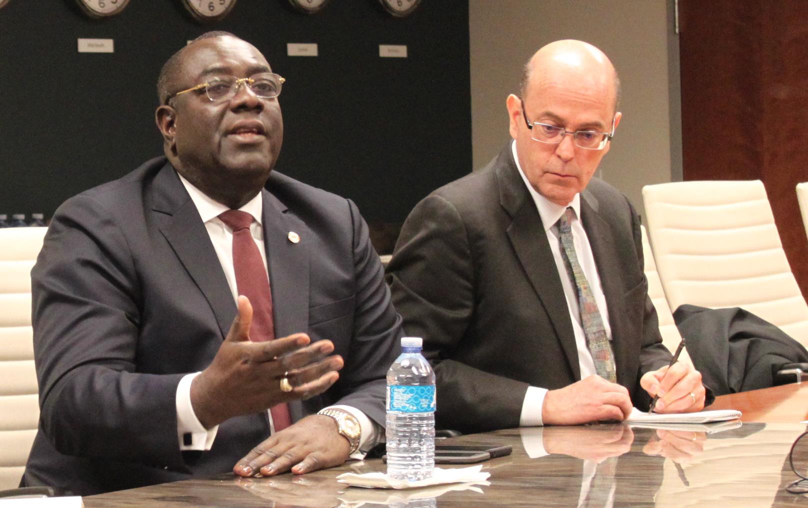 Haiti Foreign Minister Bocchit Edmond (black man wearing business suit) sits at conference table with two other men wearing business suits, wall full of clocks in background